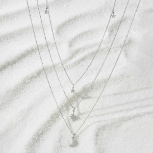 Three-layer stainless steel necklace featuring star and moon pendants on white sand