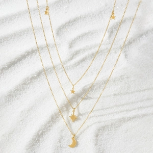 Close-up of golden layered necklace with star and moon pendants on white sand