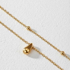 Macro view of gold teardrop pendant with bead accents on a layered anklet chain