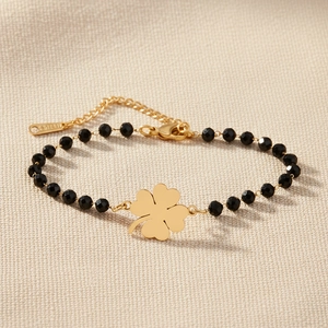 Détail des perles noires facettées et du pendentif trèfle doré sur une chaîne en acier