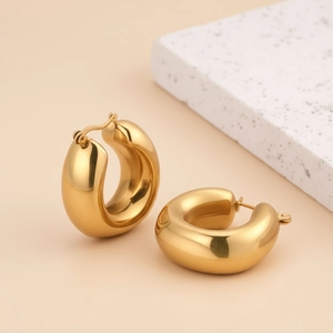 Detail of chunky gold hoop earrings with mirror polished finish on textured stone