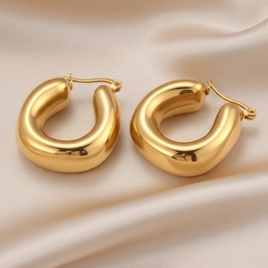 Close-up of polished golden U-shaped chunky hoop earrings on elegant silk fabric