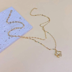 Detail of golden flower pendant with radial texture on a stylish double-layer chain