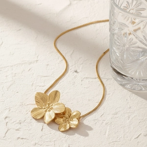 Golden double flower pendant necklace with brushed metal texture on a stone background