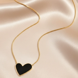 Close-up of black heart pendant with golden snake chain on elegant silk fabric background