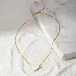 Dettaglio di una collana a catena serpente dorata con pendente a cuore bianco su marmo