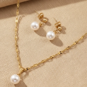 Detail von hochglänzender weißer Perlenkette und passenden Ohrringen in Gold-Optik