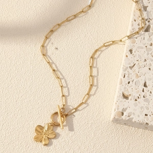 Detail of gold paperclip necklace featuring a textured flower pendant and OT toggle clasp