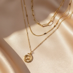 Close-up of triple-layered gold necklaces with paperclip chain and spiral pendant detail
