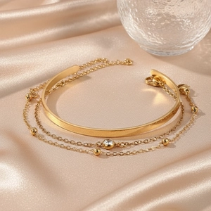 Détail de l'ensemble bracelet doré multicouche avec zircon sur fond satiné champagne