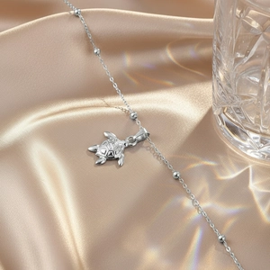 Silver stainless steel turtle pendant anklet with beads on champagne silk background