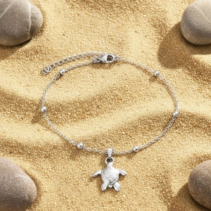 Minimalist silver stainless steel turtle charm anklet for women on a sandy beach background