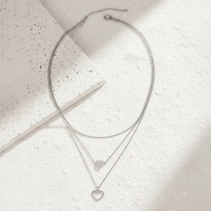 Detail of layered stainless steel necklace featuring solid and hollow heart pendants
