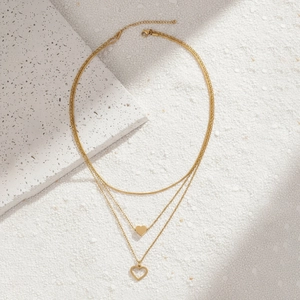 Detail of 18K gold-plated triple-layered necklace with heart pendants on sand texture