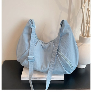 Close-up of light blue crescent tote bag with pleats and adjustable strap on a table