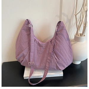 Detail view of purple pleated nylon crescent bag with adjustable strap on a dark surface