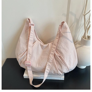 Detail of light pink pleated nylon hobo bag featuring adjustable strap and side zipper pocket