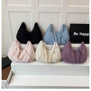 Five assorted nylon crescent shoulder bags arranged on white steps in a bright retail setting