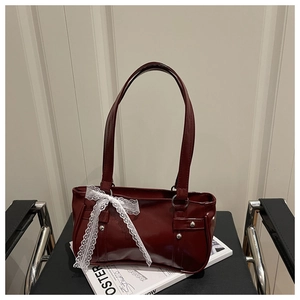 Detail of dark red patent leather bag featuring white lace bow and silver rivet accents
