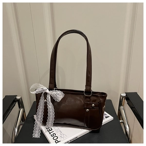 Detail of a brown glossy underarm bag with white lace bow on a studio chair