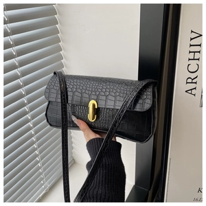 Detail of black crocodile pattern shoulder bag with golden oval twist lock and slim strap