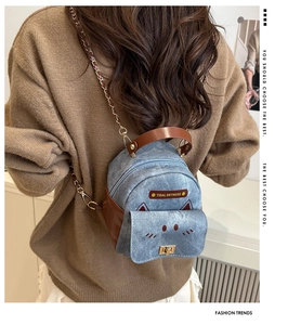 Detail of mini denim backpack featuring cat embroidery and brown leather trim on model