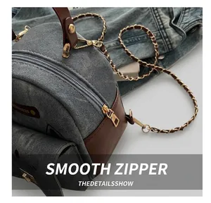 Detail of smooth metal zipper on blue denim handbag with brown leather trim and chain