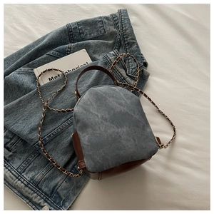 Detail of vintage denim backpack with leather trim and woven chain strap on white fabric