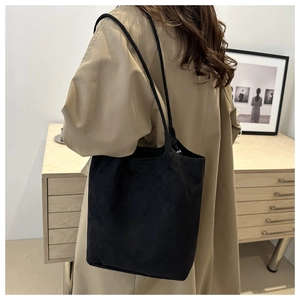 Close-up of minimalist black suede tote bag with long straps worn over a trench coat