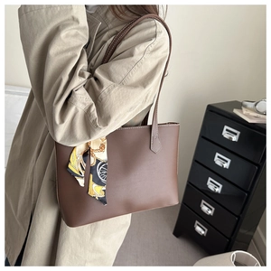 Close-up of deep brown leather tote bag with white stitching and decorative silk scarf