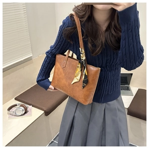 Détail d'un sac cabas en cuir caramel avec foulard en soie porté par un mannequin