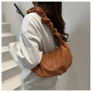 Sac hobo en daim marron avec design plissé porté par un mannequin sur une épaule