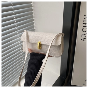 Detailed close-up of cream crocodile pattern underarm bag with gold oval metal lock