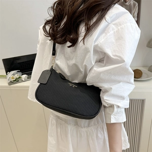 Chic black underarm bag with diagonal pattern and gold chain strap on a white dress model