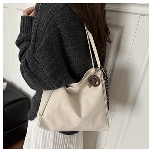 Minimalist cream shoulder bag with contrast charms worn with a knit sweater and skirt