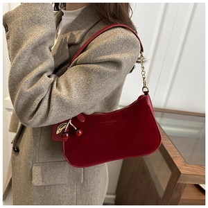 Detail of red vintage underarm bag with cherry charm and gold chain strap on model