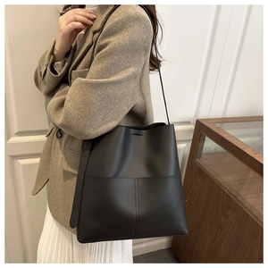 Detail of a black matte leather tote bag worn by a model against a minimalist white door