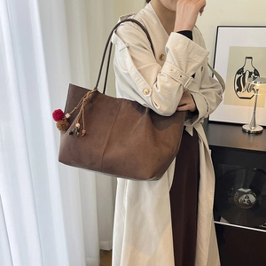 Large brown suede tote bag with decorative tassel shown in a stylish room setting