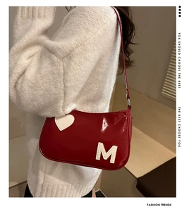 Detail of red patent leather shoulder bag with white M letter and heart patch