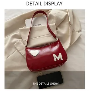 Detail view of burgundy underarm bag with white heart and M letter embroidery