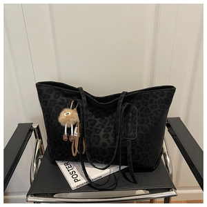 Détail d'un grand sac cabas léopard noir avec un pompon en peluche marron sur chaise