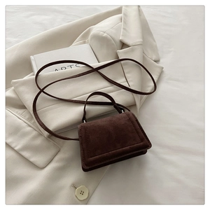 Detail of dark brown suede crossbody bag styled on a beige blazer and art book