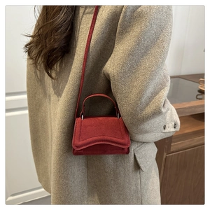 Detail of red suede mini crossbody bag with wavy flap shown on a grey wool blazer