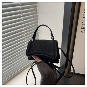 Close-up of black matte suede mini handbag with metal handle and thin shoulder strap