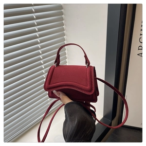 Detail of burgundy suede mini handbag with rounded handle and fine shoulder strap