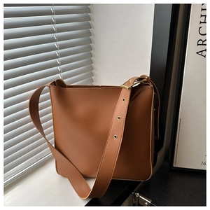 Detailed close-up of brown leather bucket bag with wide strap and gold metal eyelets