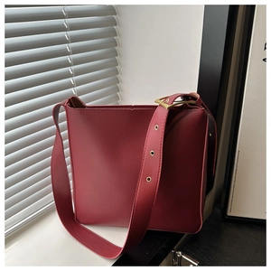 Close-up of deep red leather bucket bag featuring wide eyelet strap and golden buckle