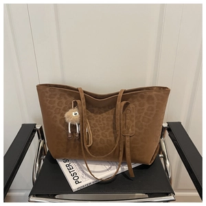 Détail d'un sac cabas marron à motif léopard avec pompon en peluche sur une chaise