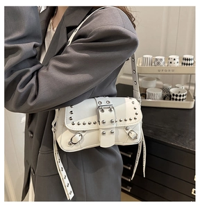 Detail van een witte punk schoudertas met zilveren metalen noppen en verstelbare riem