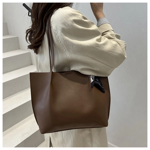 Detail of a brown leather tote bag with a decorative floral scarf on the handle